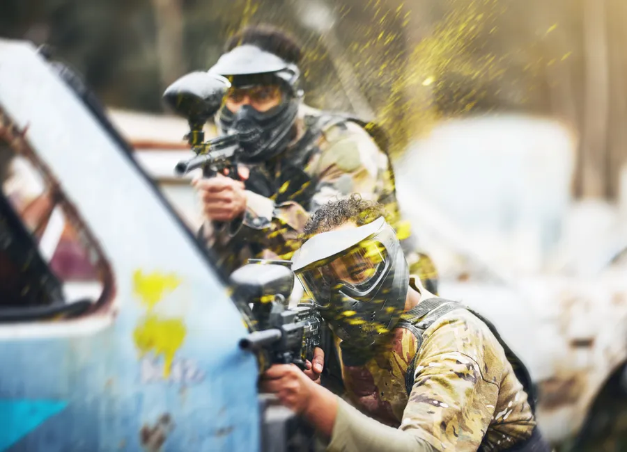 Paintball players in masks taking cover