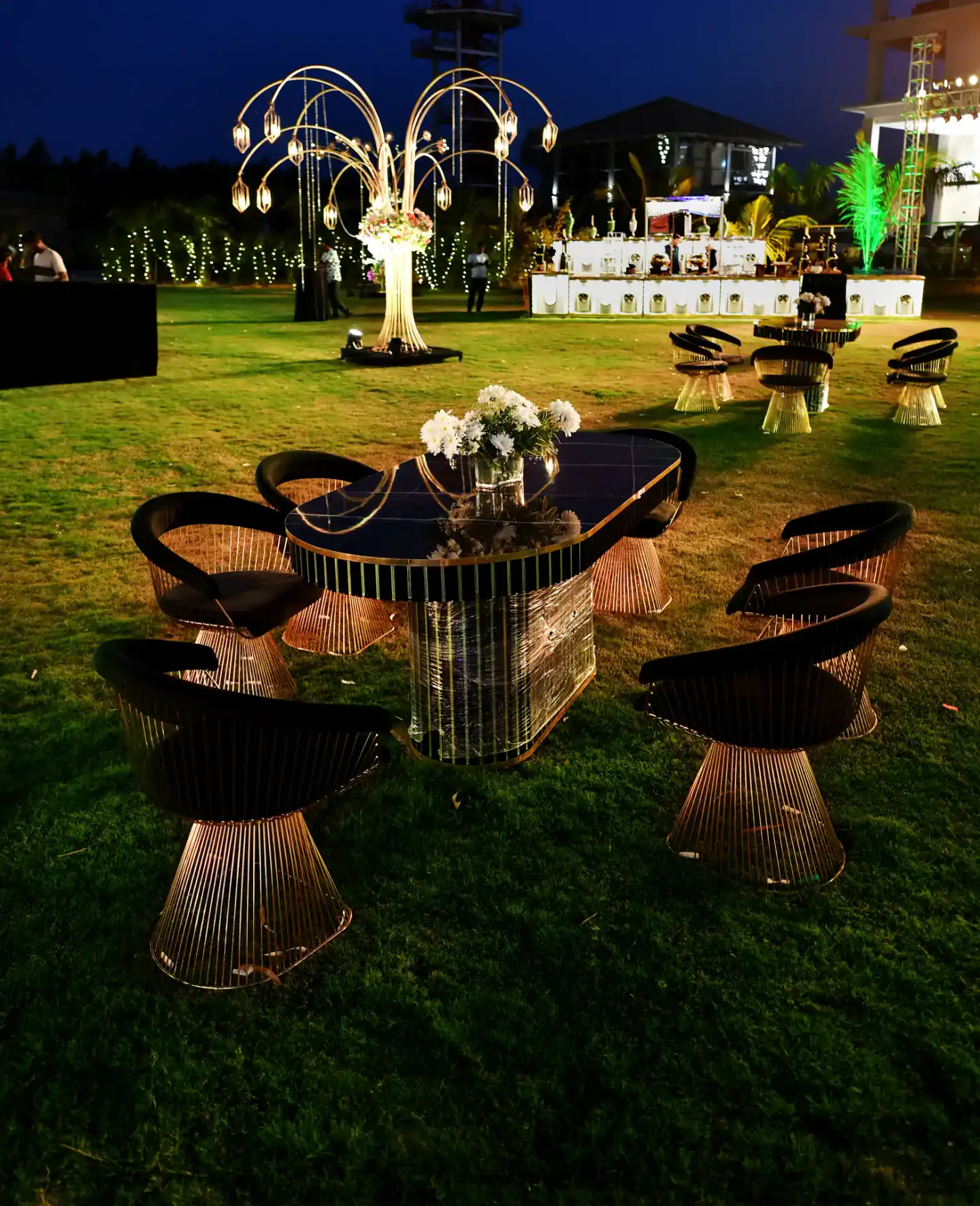 Gold lamp trees and dining tables at a night wedding on the lawn
