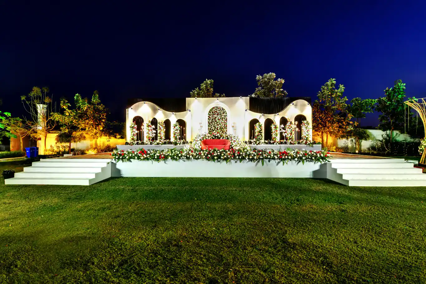 White arched wedding stage lit at night on the lawn at Sportico Resorts